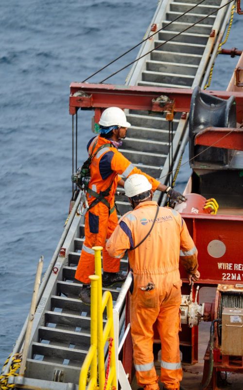 Offshore male workers in orange uniforms maintaining an oil rig at sea.